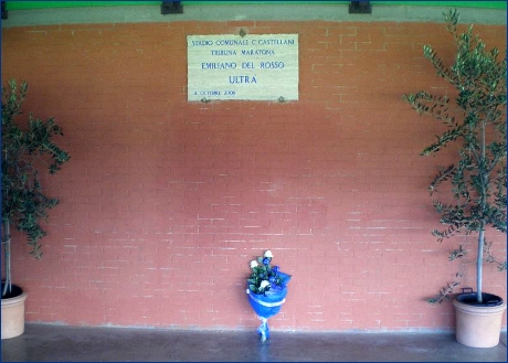 Targa che intitola la tribuna Maratona dello stadio Castellani di Empoli ad Emiliano Del Rosso con a terra un mazzo di fiori bianchi e azzurri